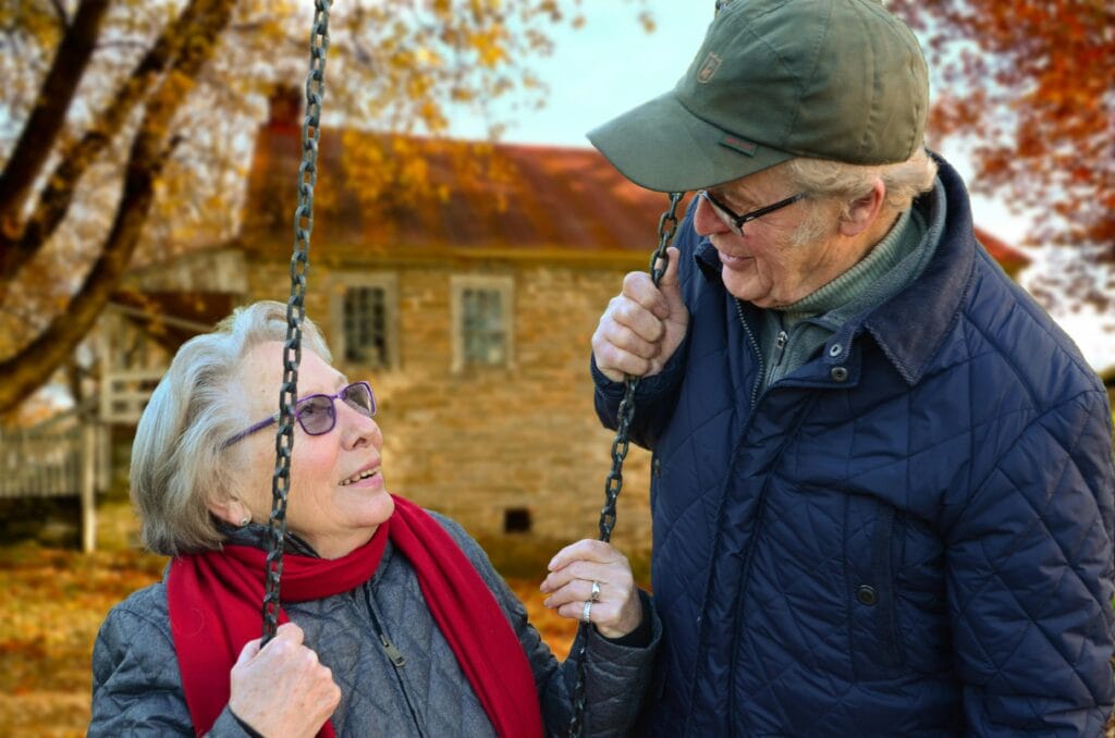 old-people-couple-together-connected-34761 A happy elderly couple sharing a joyful moment on a swing in autumn setting.